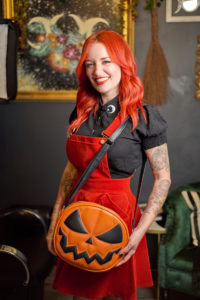 Karina standing in her suite holding a pumpkin purse.
